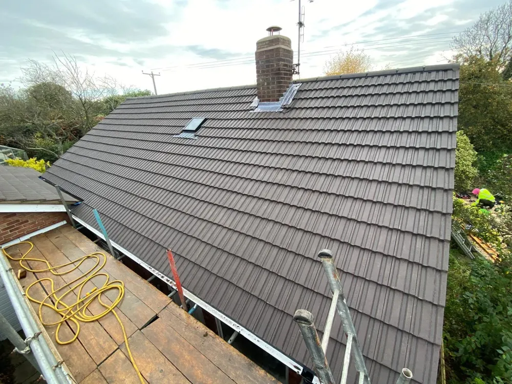 A newly tiled roof with a roof window and chimney, seen from the scaffold