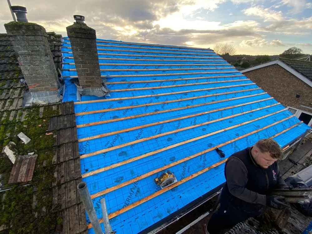 A Prestige roofer working on a roof stripped back to new blue membrane and battens